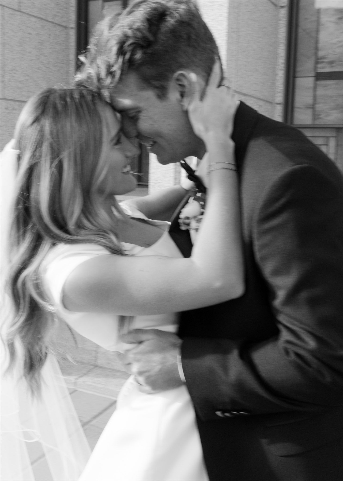 A bride and groom sharing a joyful close embrace in a romantic black and white wedding portrait.