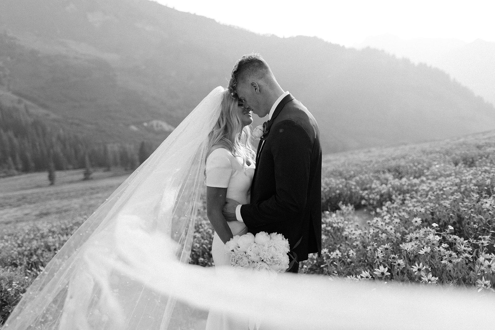 A bride and groom sharing an intimate moment in a stunning mountain meadow with a flowing veil.